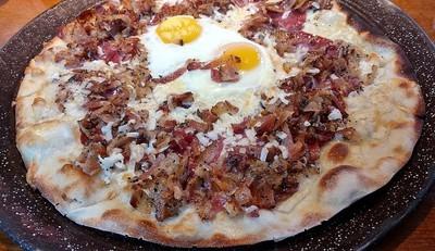 Croque Madame Brick Oven Pizza a French traditional pizza, gruereand locatelli cheeses, artisan sopressata, bacon and a sunny-side egg.